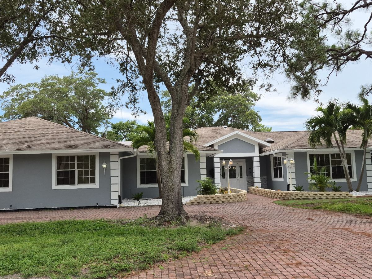 The front of KIVA at Canterbury in Bonita Springs, Florida — a single-storey building with a covered entry, framed by a large oak and palm trees