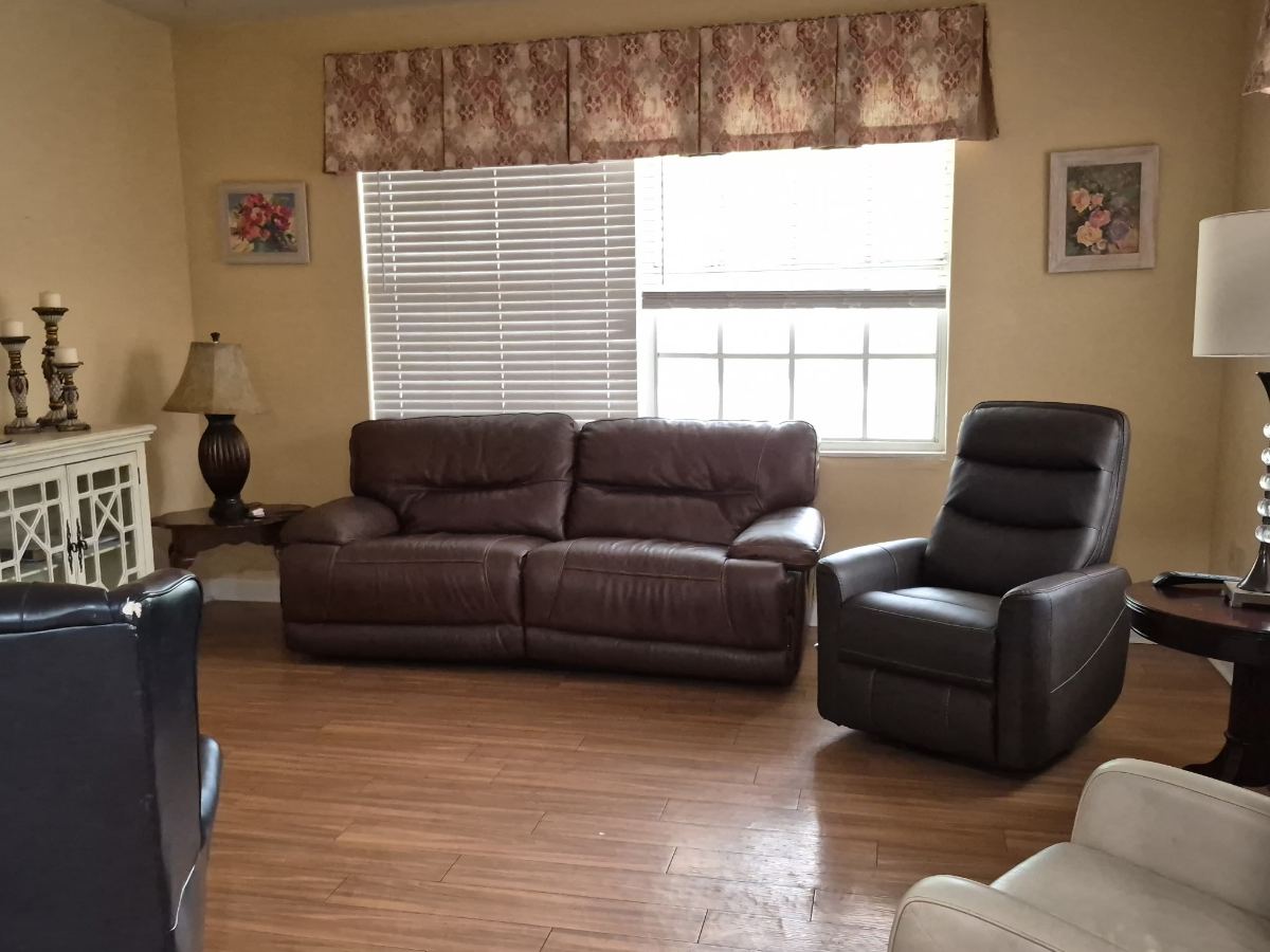 A living room with brown leather sofa and recliners beside a wide curtained window